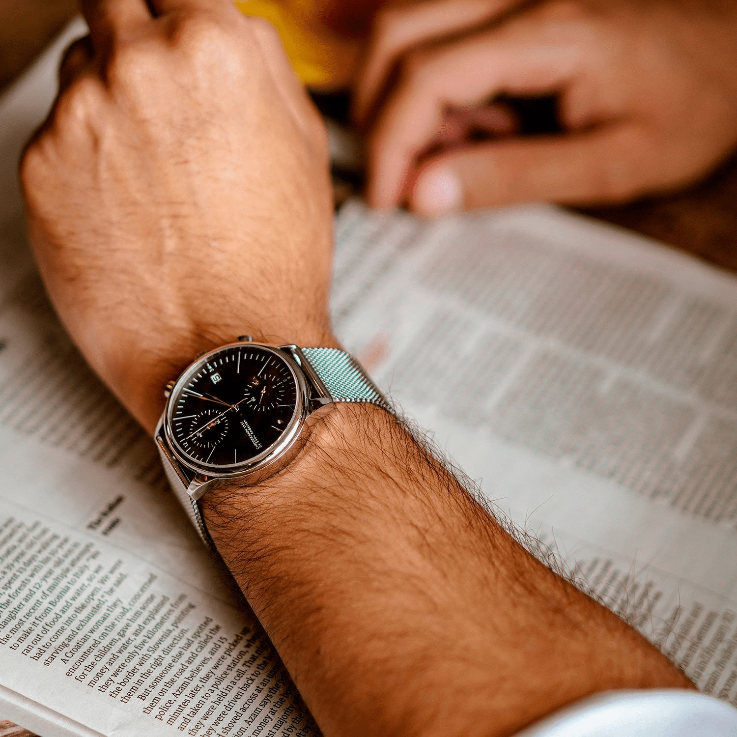 1844 Chronograph d'AV86 avec cadran d'inspiration vintage, Fonction chronographe, Verre saphir et bracelet en mailles métalliques, porté par une personne lisant le journal