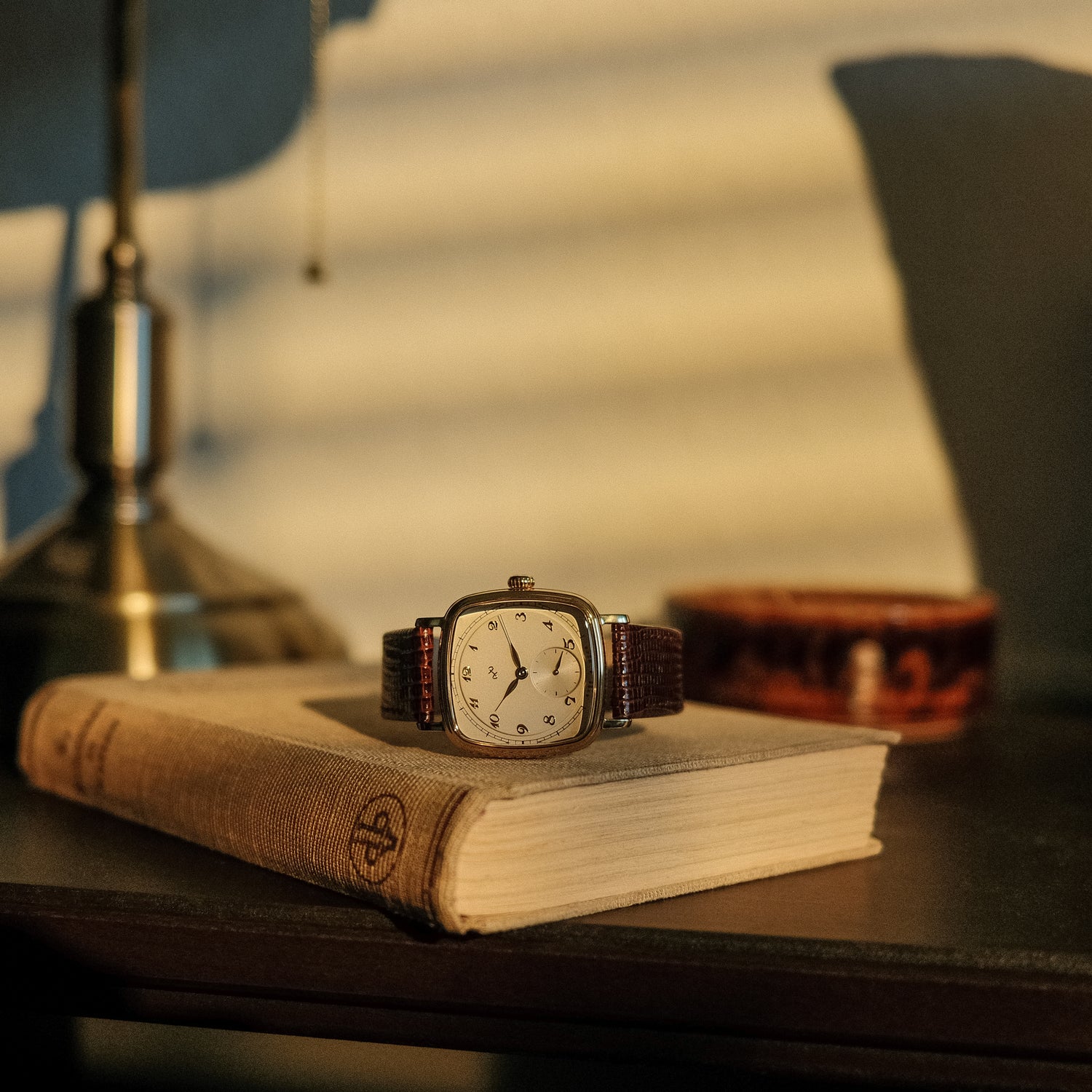 1954 Amalfi Mechanical by AV86 on vintage book with warm light, highlighting cushion case and leather strap in classic setting