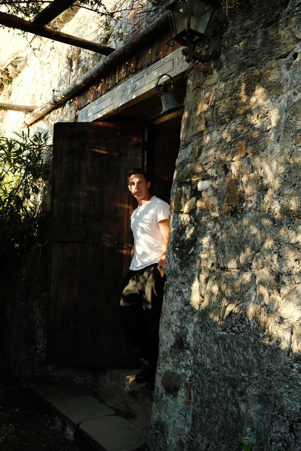 Man in minimalist casual wear standing in rustic Mediterranean doorway, wearing 1954 Amalfi Mechanical, Gold / Midnight Blue by AV86