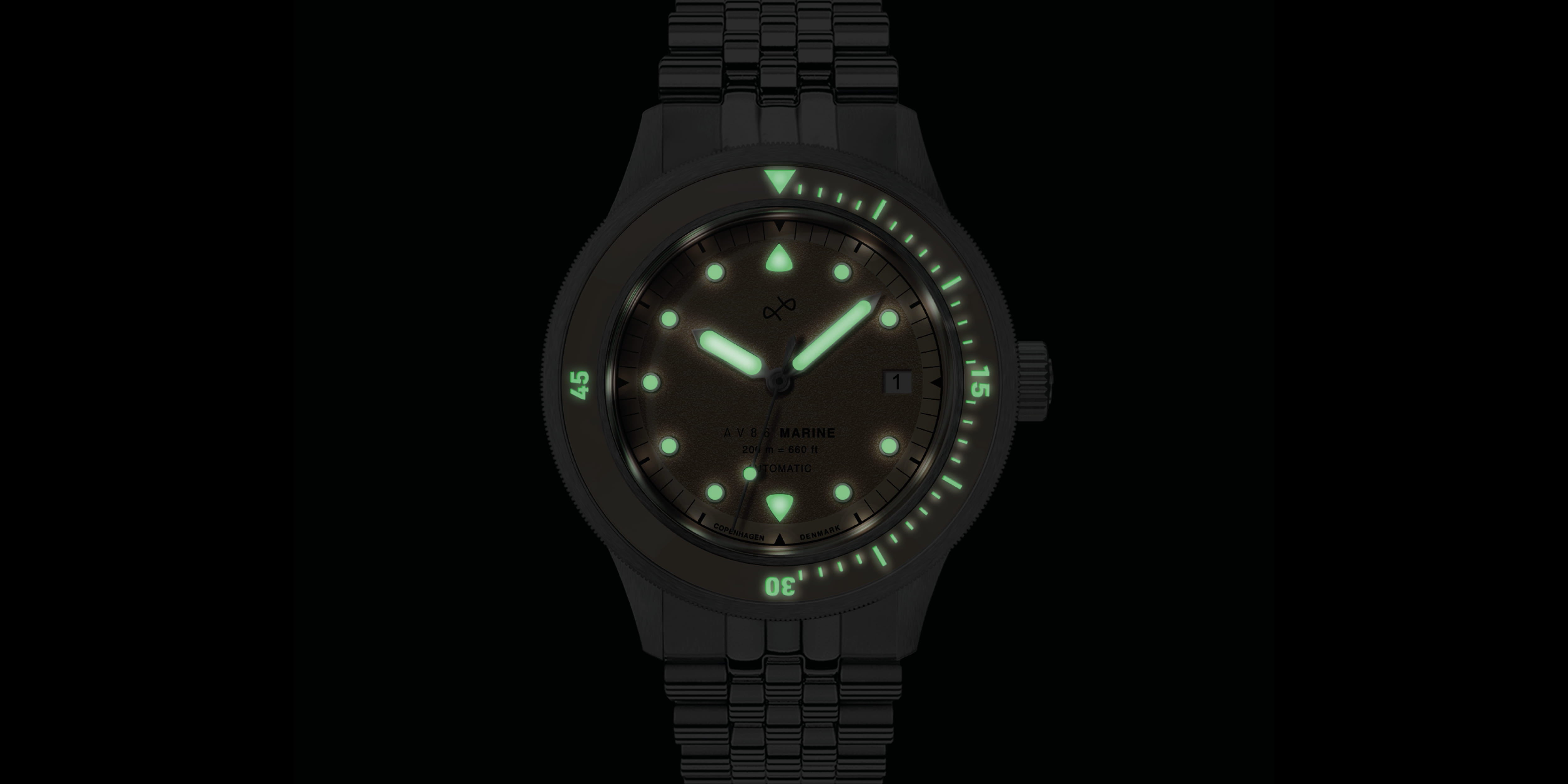 Dark background with a wristwatch showing luminescent green markers, hands, and bezel indicators on a metal bracelet.