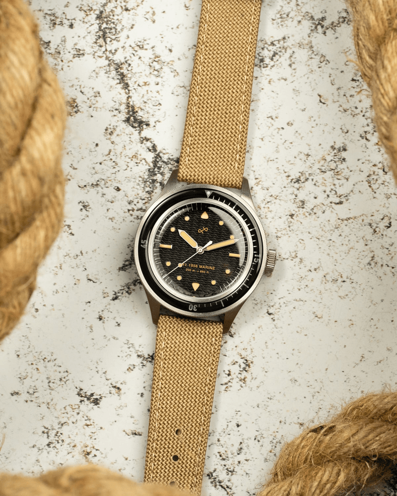 1956 Marine by AV86 vintage-inspired diver with acrylic bezel, textured black dial, luminous markers, and beige fabric strap