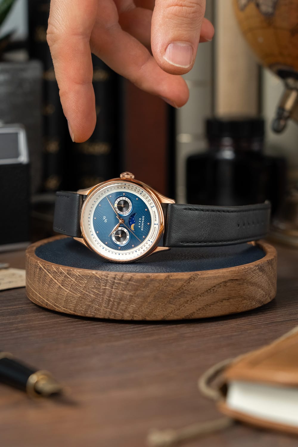 1968 Moonphase, Rose Gold / Dark Blue by AV86 luxury moonphase watch with sapphire crystal and black leather strap on wooden stand