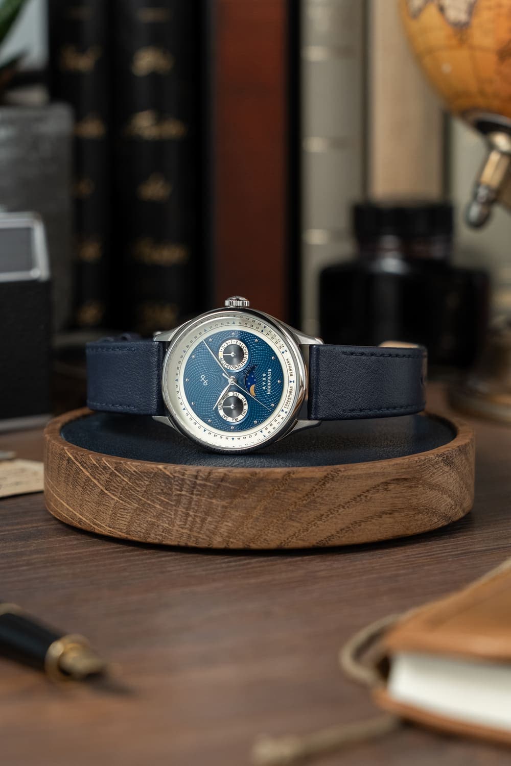 AV86製「1968 Moonphase」高級ムーンフェイズ時計。サファイアクリスタル、ヴィンテージ風の文字盤、ダークレザーストラップ付き。木製スタンドに載せてあります。