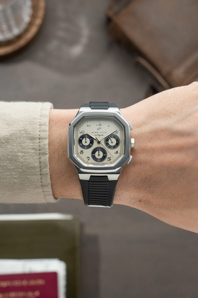 The 1904 Chrono by AV86 features a vintage-inspired chronograph dial with three subdials, set in a polished square steel case paired with a modern rubber strap, embodying Danish design and horological excellence.