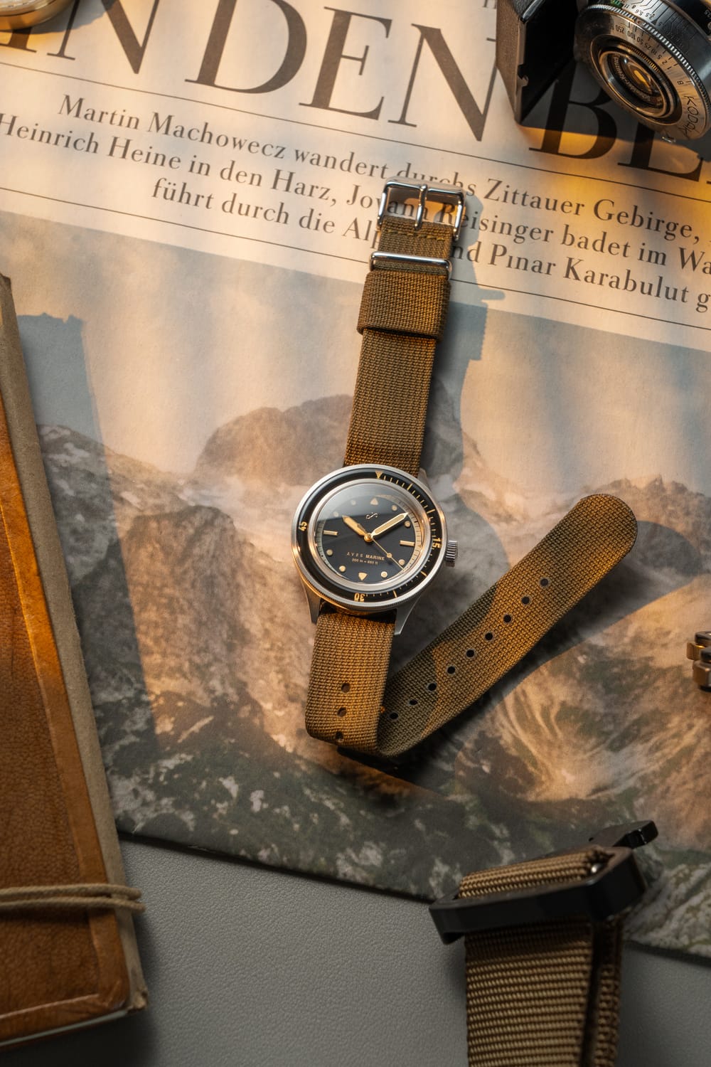 1956 Marine by AV86 vintage-inspired diver with sapphire crystal, compass bezel, and textured fabric strap on newspaper backdrop