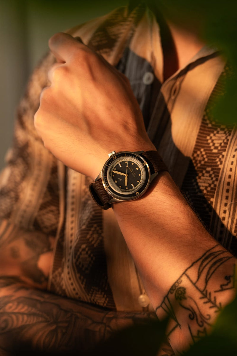 1956 Marine by AV86 vintage-inspired diver watch with sapphire crystal, compass bezel, and textured rubber strap on wrist in warm light