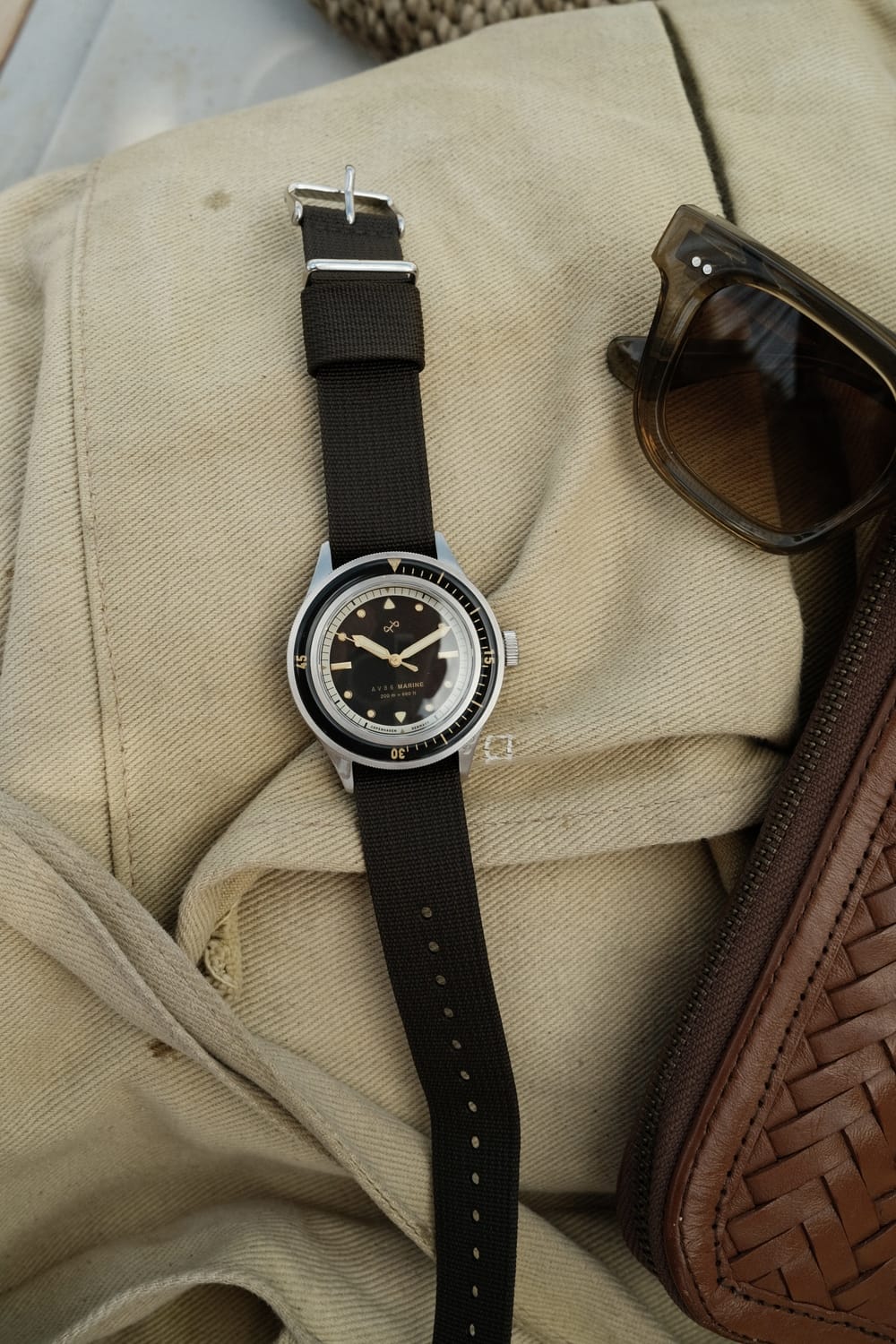 1956 Marine by AV86 vintage-inspired diver with sapphire crystal, compass bezel, and black fabric strap on beige fabric background
