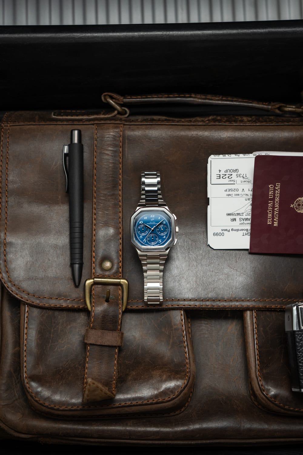 1904 Chronograph by AV86 with angular case, sapphire crystal, chronograph dial, and brushed metal bracelet strap on leather bag