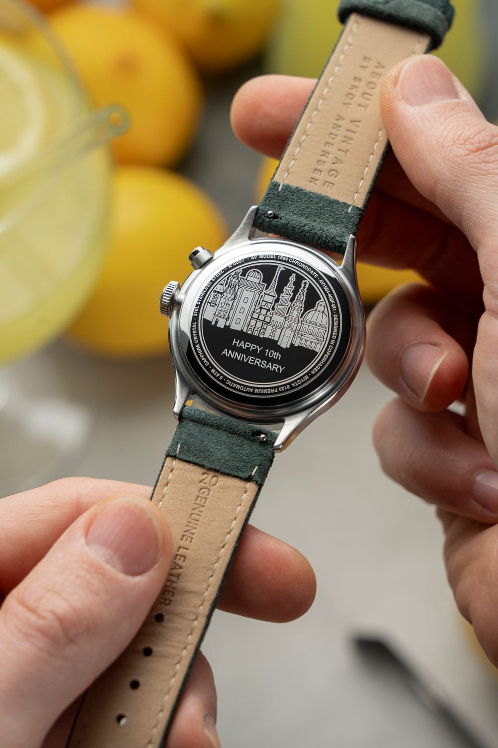 Hands holding AV86 watch with engraved case back celebrating 10th anniversary, genuine leather strap, Scandinavian design elements