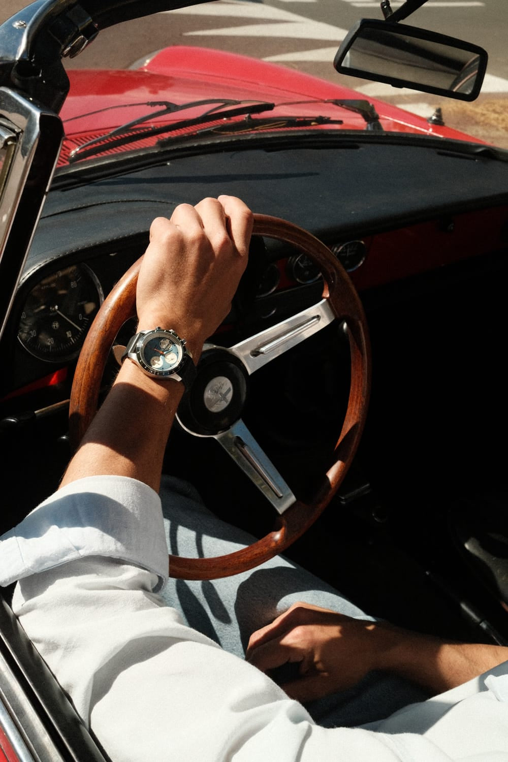 AV86 1960 Racing Chronograph, Steel / Sky Blue & Green quartz watch with chronograph dial on wrist while driving a vintage red car