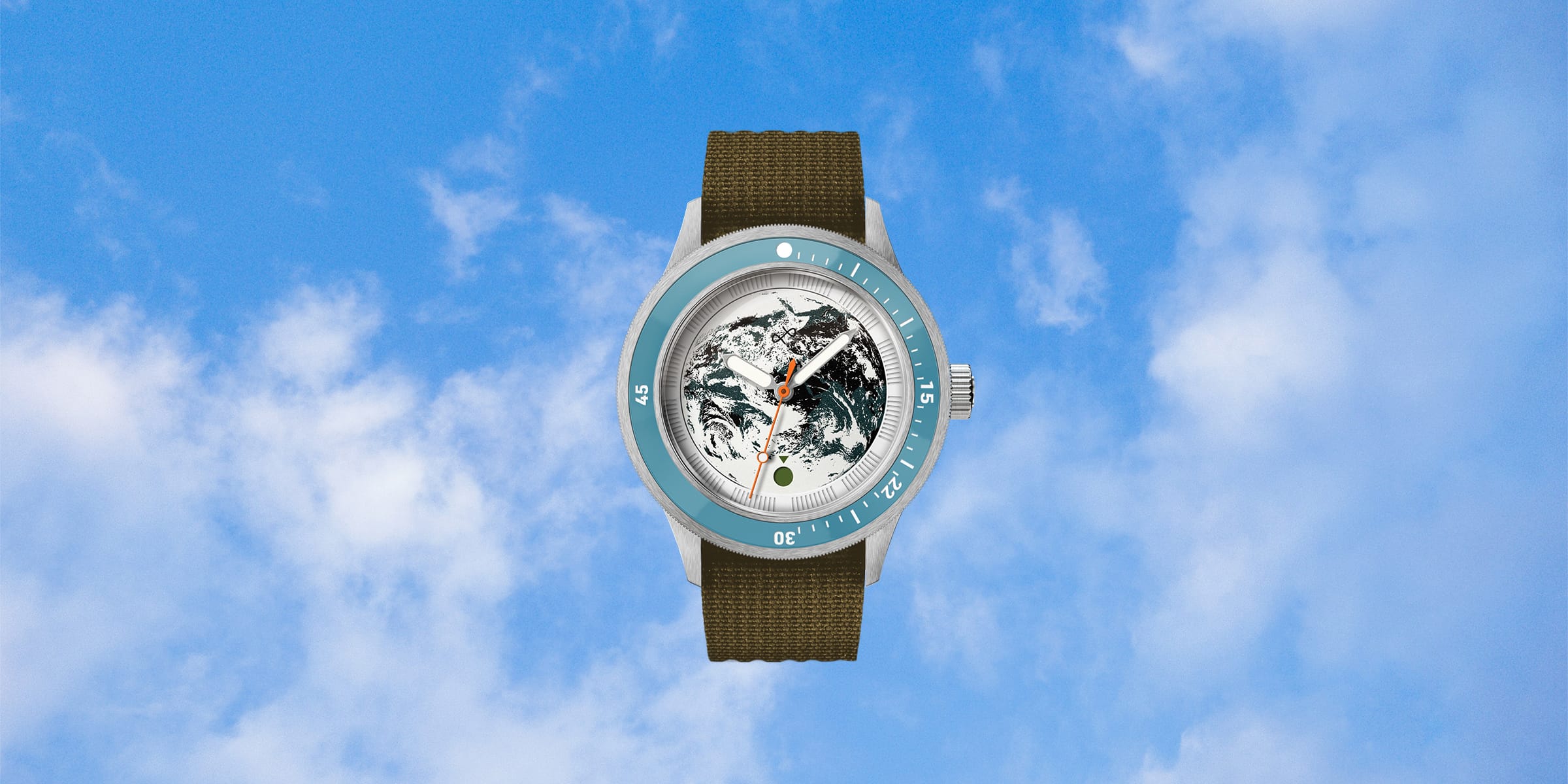 Wristwatch with Earth-themed dial, light blue bezel, and olive green textured strap against bright blue sky with scattered clouds.