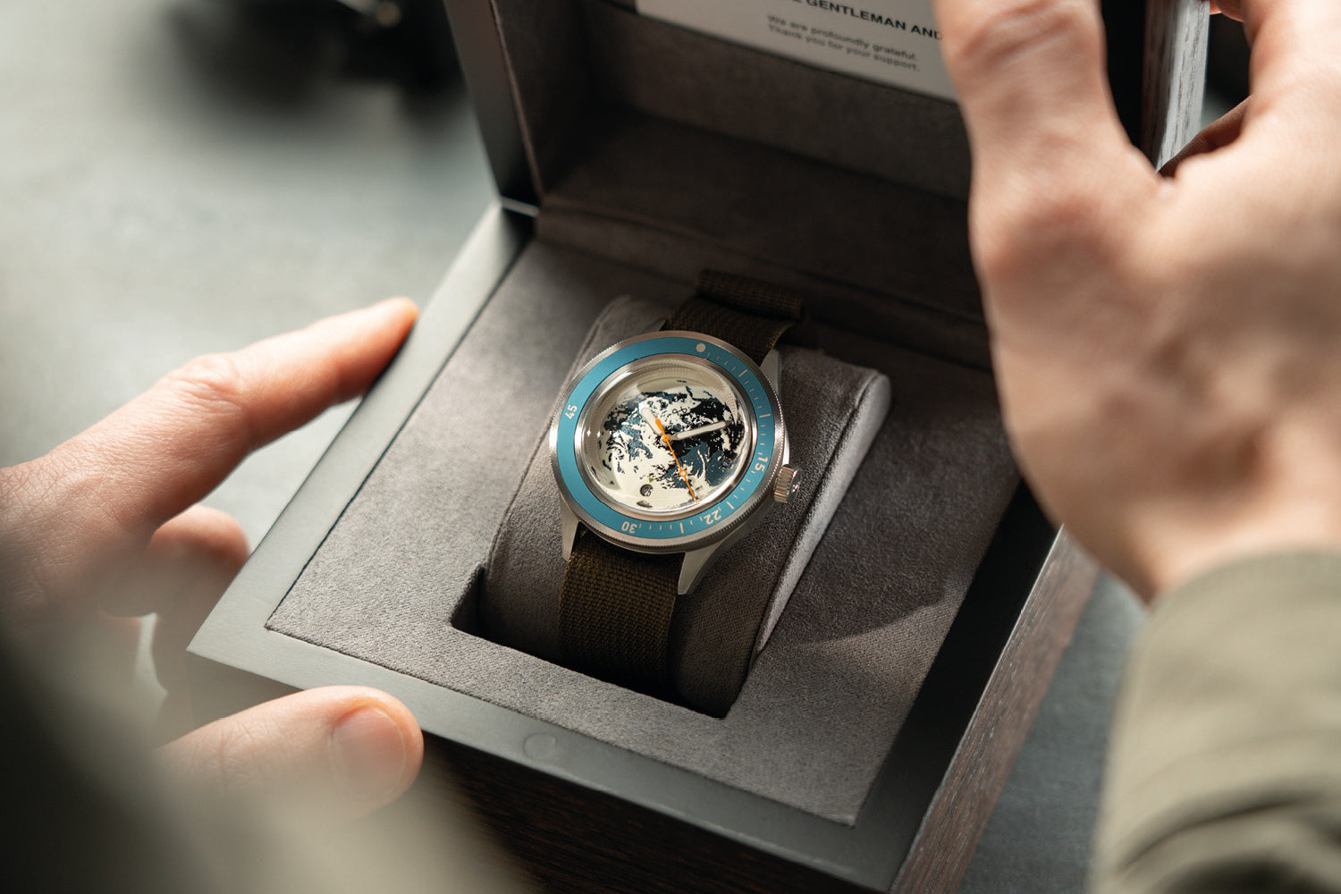 AV86 automatic watch with exposed mechanical movement, textured dial, and dark woven strap presented in a lined watch box