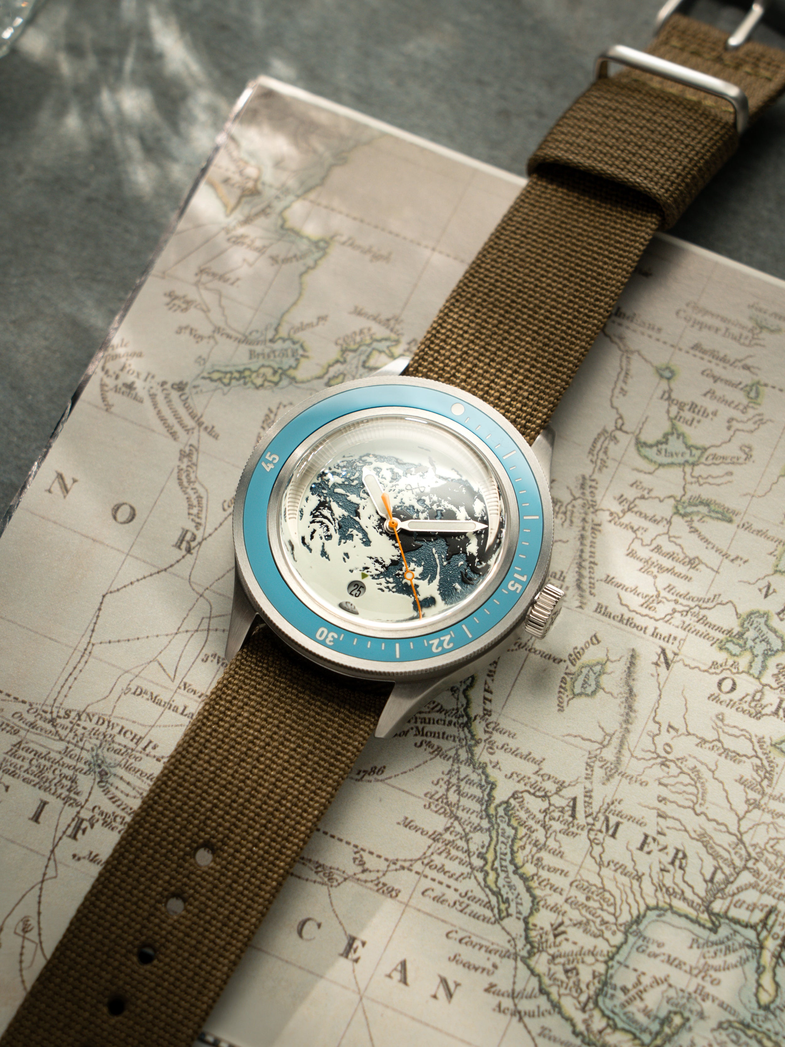 Wristwatch with blue bezel, detailed globe dial, and brown fabric strap resting on an antique world map surface.