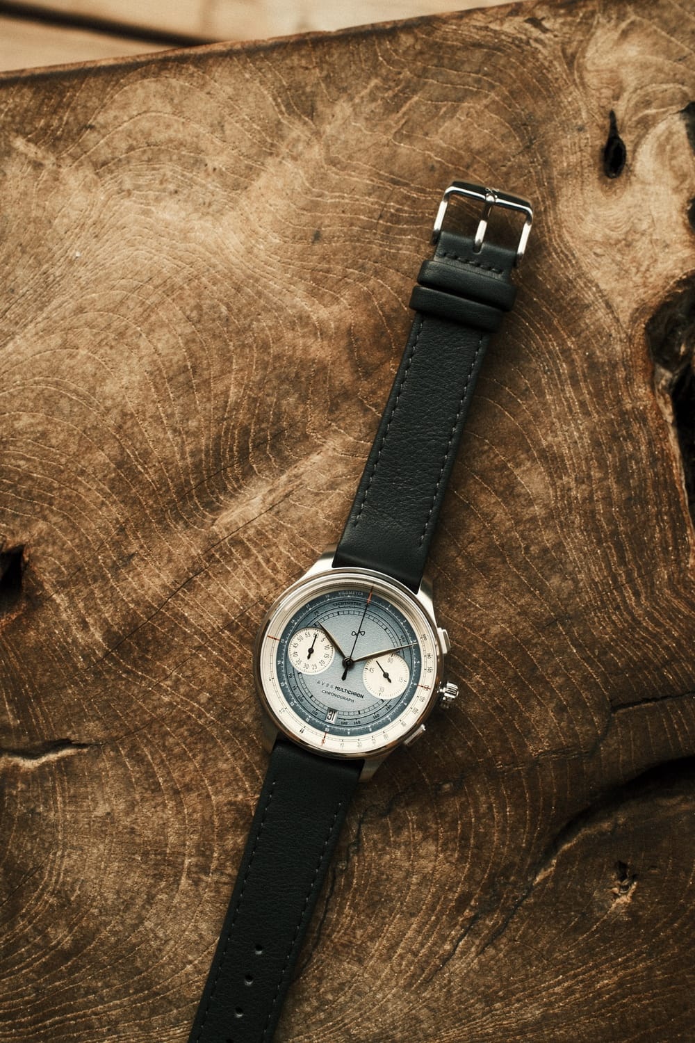 AV86 1934 Multichron, Steel / Sky Blue quartz chronograph with detailed dial and black leather strap resting on a rustic wood surface