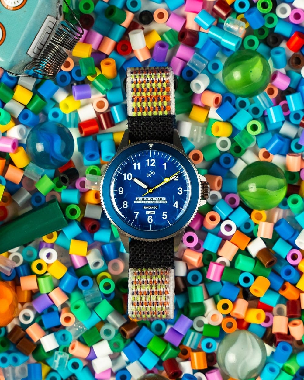 AV86 diver wristwatch with blue Arabic numeral dial, black rotating bezel and multicolored woven strap arranged among colorful beads and glass marbles