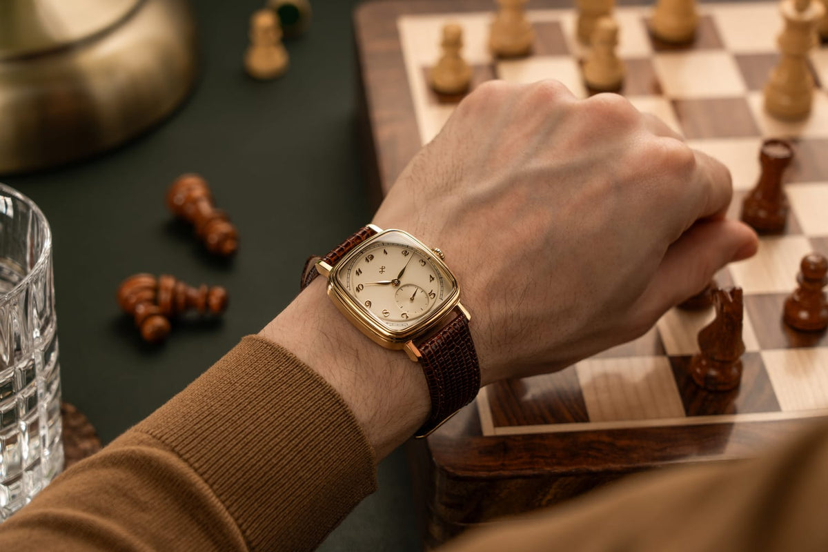 Wrist wearing AV86 dress watch with cushion case, vintage-inspired dial, mechanical small seconds, and textured leather strap by chessboard.