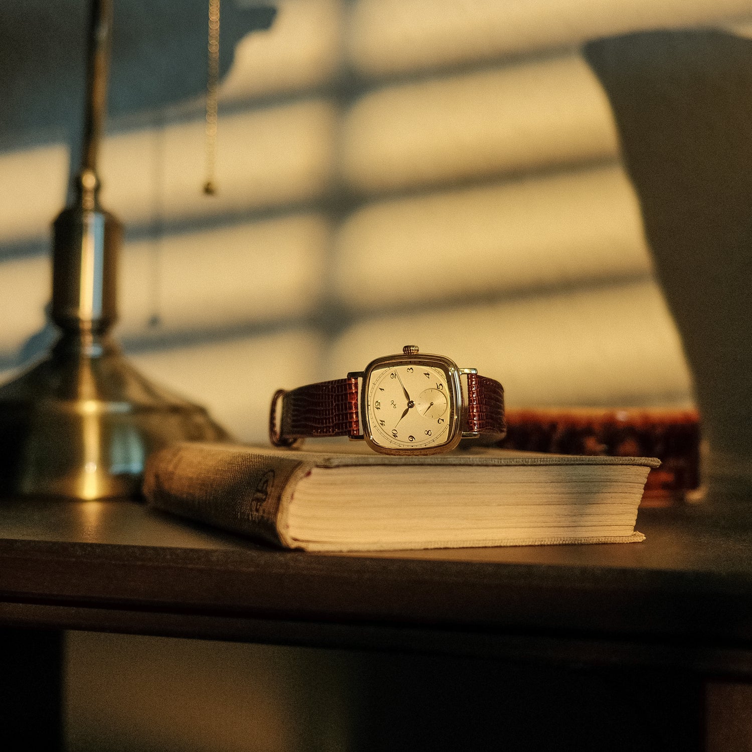 AV86 vintage-inspired dress watch with cushion case, mechanical small seconds, and textured leather strap resting on a book by soft sunset light