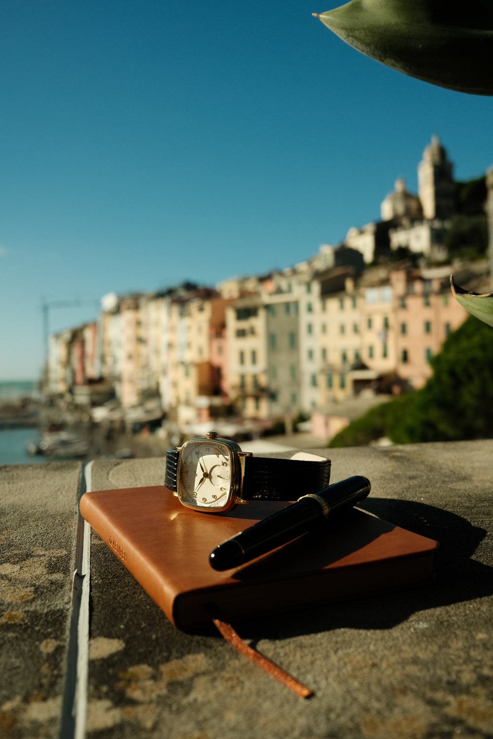 AV86 vintage-inspired dress watch with cushion case and mechanical dial resting on leather journal beside fountain pen by Mediterranean harbor.