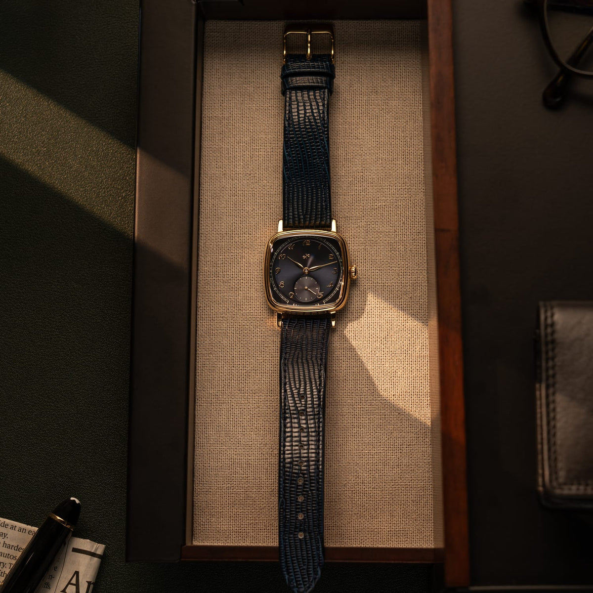 AV86 dress watch with cushion case, mechanical small seconds, textured leather strap resting in wooden tray with soft shadow play
