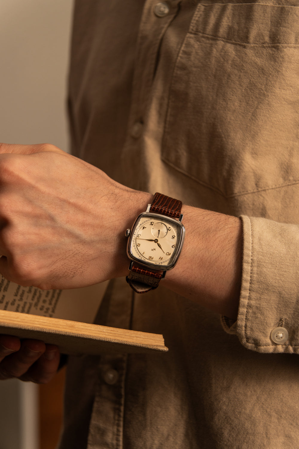 1954 Amalfi Mechanical by AV86 with cushion case, vintage dial, mechanical movement, and textured brown leather strap on wrist reading book