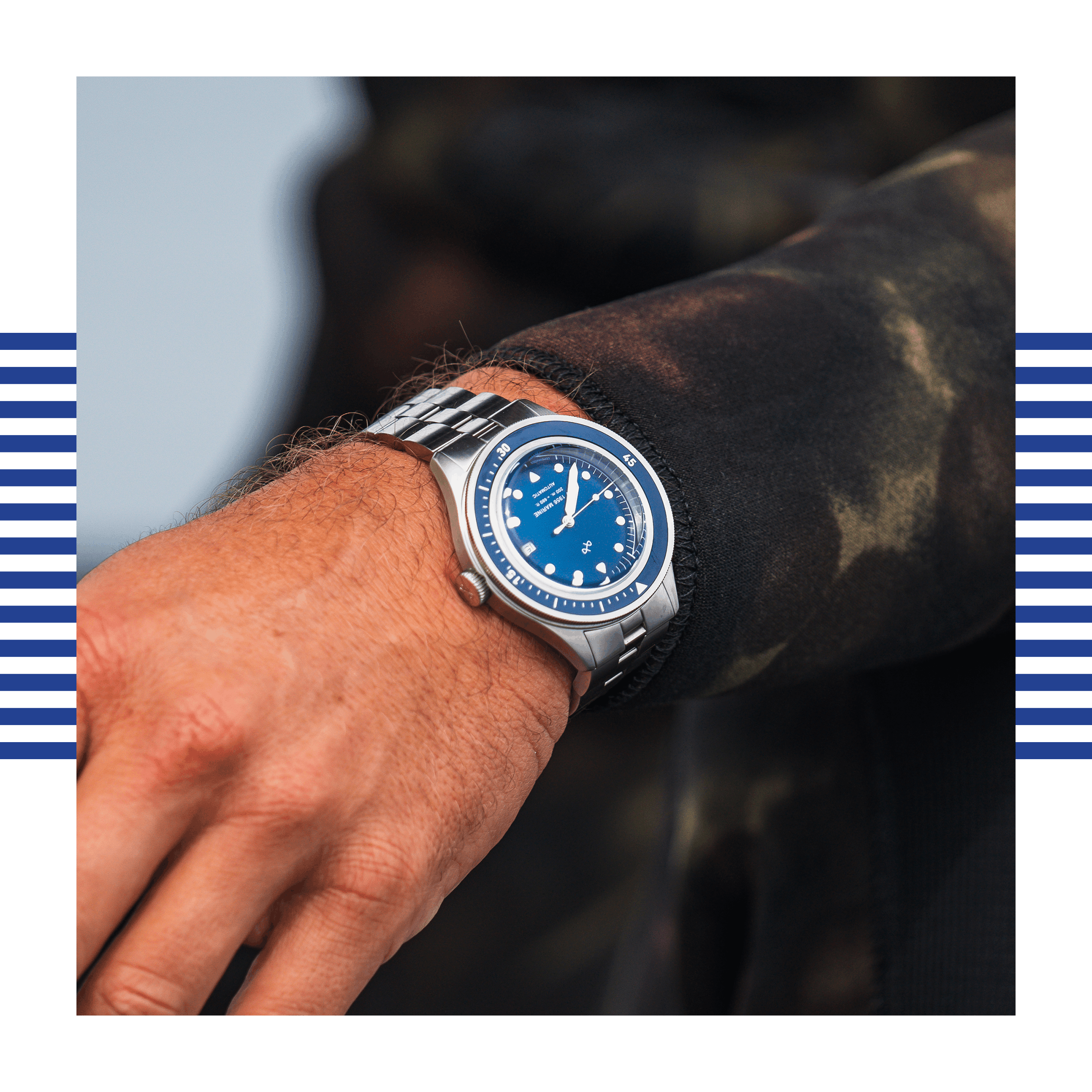 Close-up of wrist wearing a stainless steel watch with a blue dial and rotating bezel against a blurred dark background.