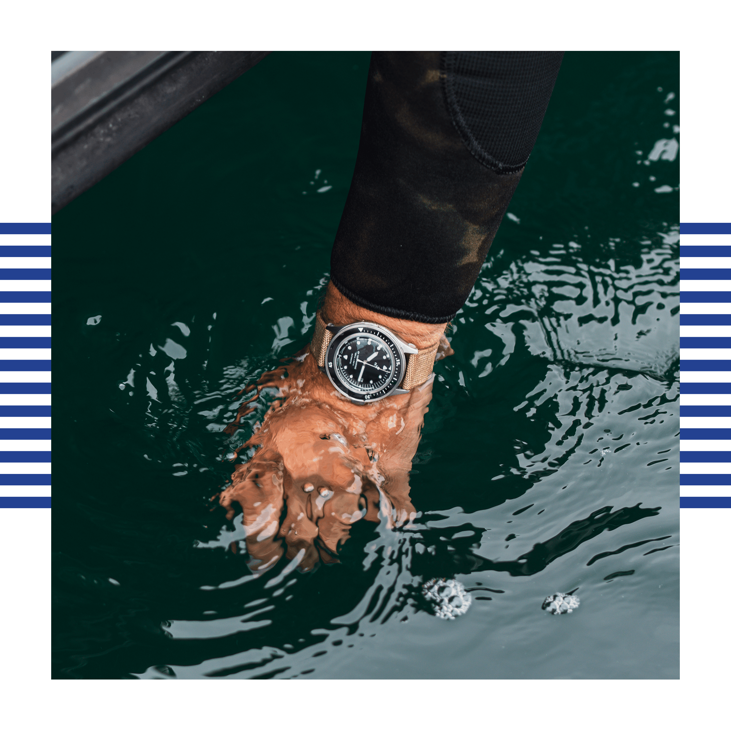 Wrist submerged in water wearing a steel watch with a black dial and rotating bezel on a diver’s suit sleeve.