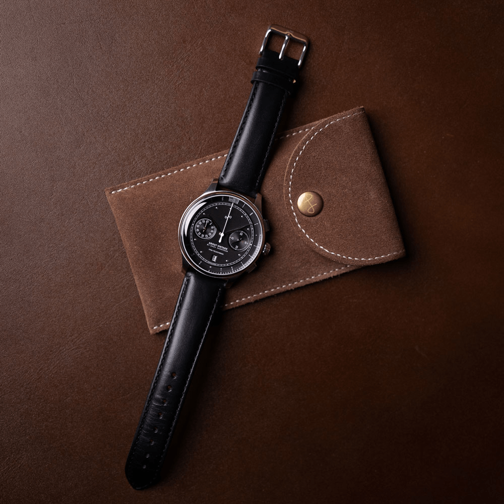 1934 Telechron by AV86 features a refined chronograph with a black dial, dual subdials, date window, polished steel case, sapphire crystal, and a smooth black leather strap resting on a brown suede pouch, embodying Danish design and Nordic minimalism.