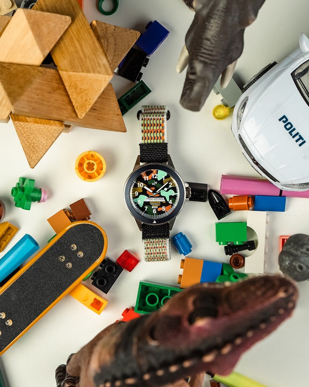 AV86 round wristwatch with colorful Arabic numeral dial, black bezel and woven strap surrounded by wooden toys, building blocks and dinosaur figures