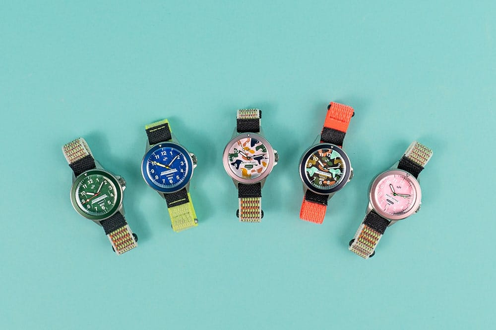 Five AV86 wristwatches with colorful dials and woven straps arranged in a row against a turquoise background, showcasing Nordic minimalism