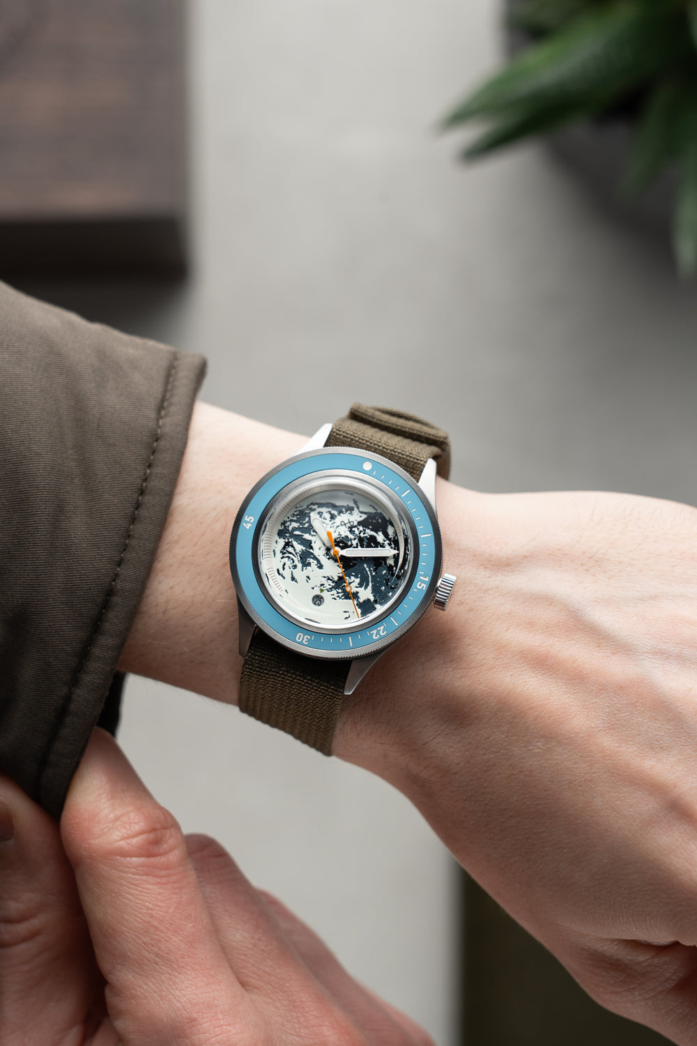 Earthrise WWF Partnership, Automatic / 2026 Edition by AV86 on wrist with a green fabric strap and blue bezel luxury timepiece.