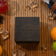 A minimalist AV86 wooden watch box set on a teak surface surrounded by fresh citrus fruits, sunglasses, a blue and brown striped fabric bag, scattered ice cubes, and a red cocktail evoking a refined Scandinavian summer lifestyle and complementing the 1564 Chronodate Automatic, Steel / Ice Blue & White packaging.