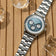 1564 Chronodate Automatic with a polished bracelet and ice blue dial featuring three chronograph subdials, presented by AV86 on a natural wood surface with melting ice cubes, conveying a blend of precision and Scandinavian minimalism.