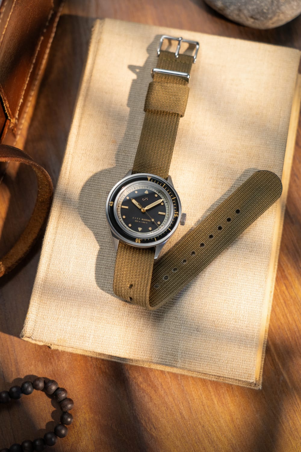 1956 Marine by AV86 vintage-inspired diver with sapphire crystal, compass bezel, and durable fabric strap on book surface