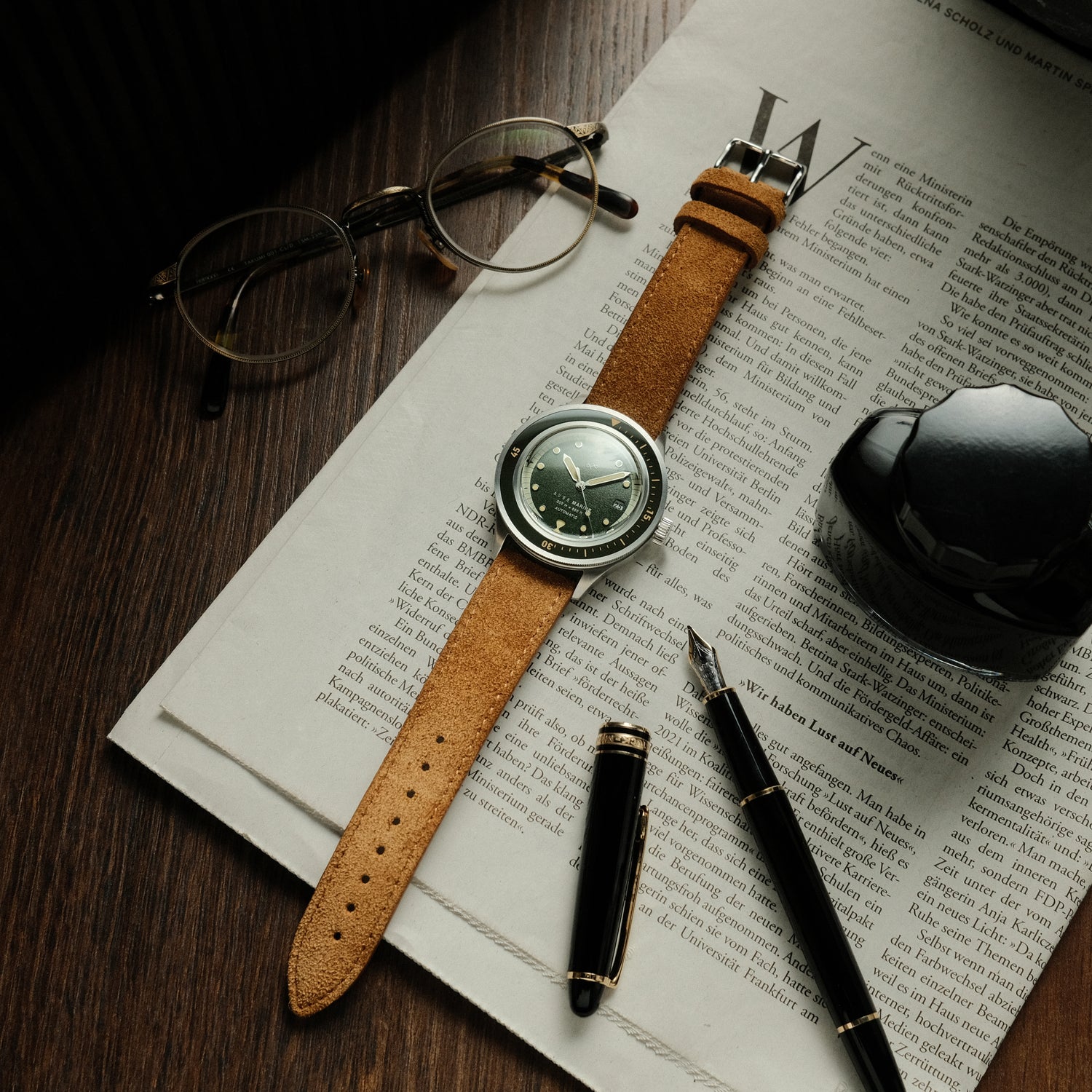 1956 Marine Automatic, Steel / Green watch with brown leather strap by AV86 on newspaper with glasses and fountain pen nearby