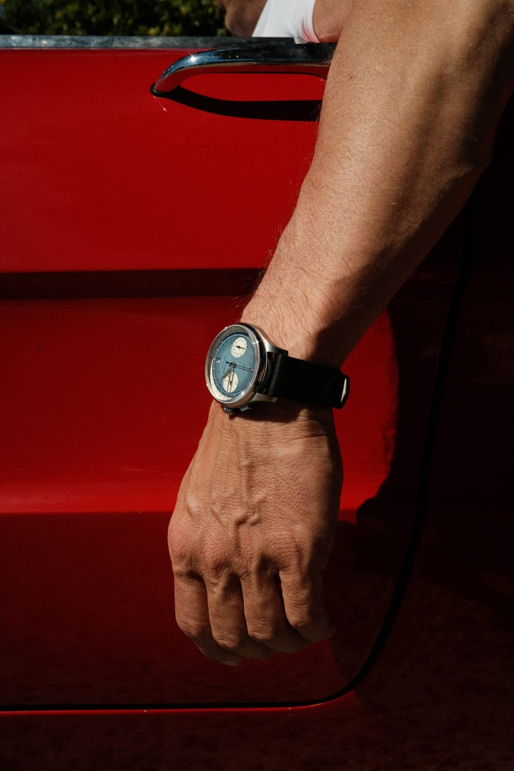 AV86 1934 Multichron, Steel / Sky Blue chronograph with pale blue dial and black leather strap worn beside a vintage red car