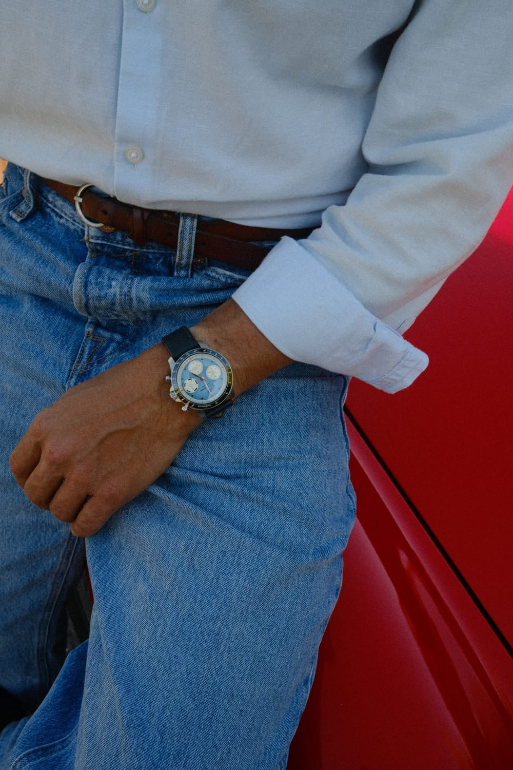 AV86 1960 Racing Chronograph, Steel / Sky Blue & Green quartz watch worn with a light blue shirt and jeans beside a red car