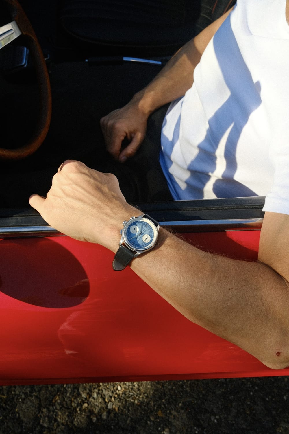 AV86 1934 Multichron, Steel / Sky Blue quartz chronograph with blue dial and black leather strap, worn beside a red classic car in sunlight