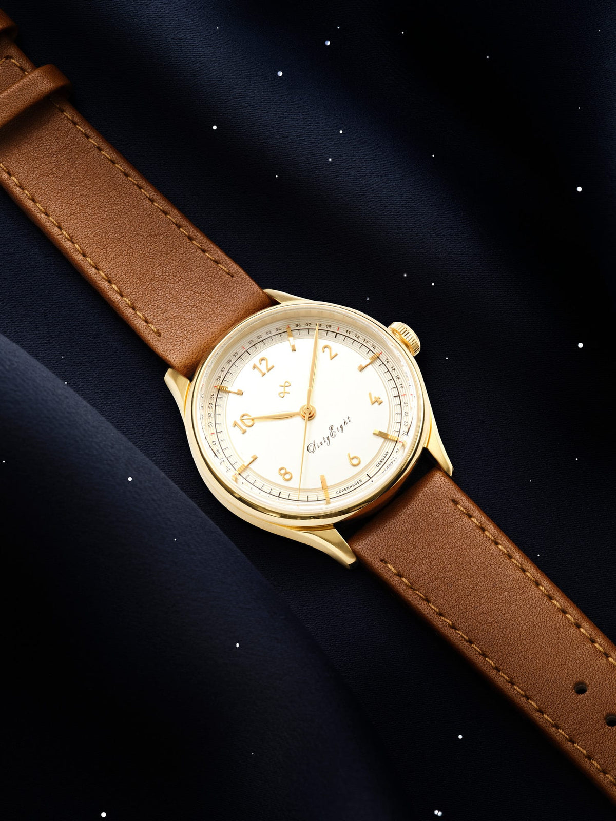 1968 Sixtyeight by AV86 vintage-inspired dress watch with sapphire crystal, gold case, and brown leather strap on dark textile background